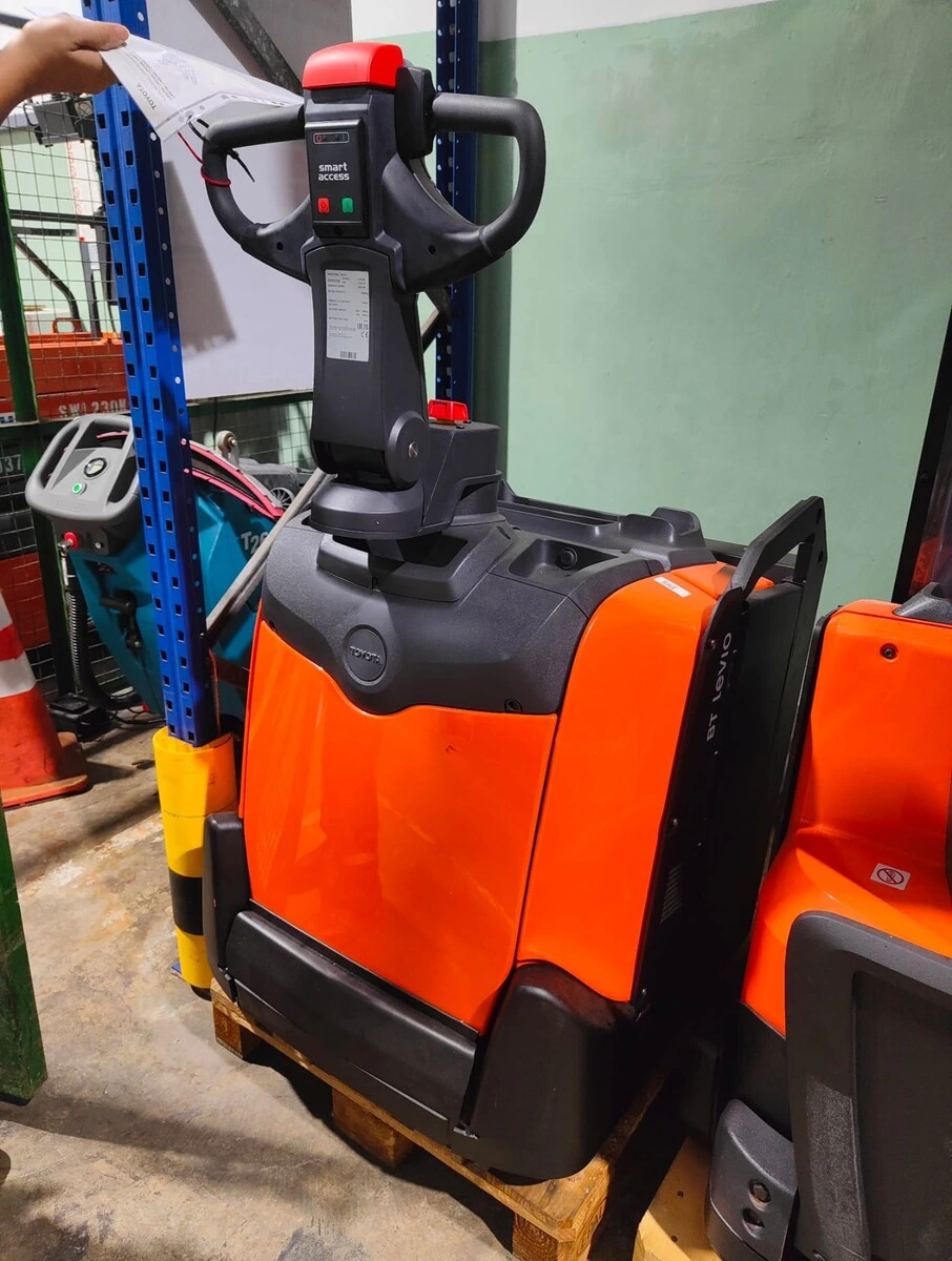 Inspection of a Powered Pallet Truck A warehouse worker in Singapore is inspecting a paperwork note attached to the handle of a Toyota electric pallet jack.