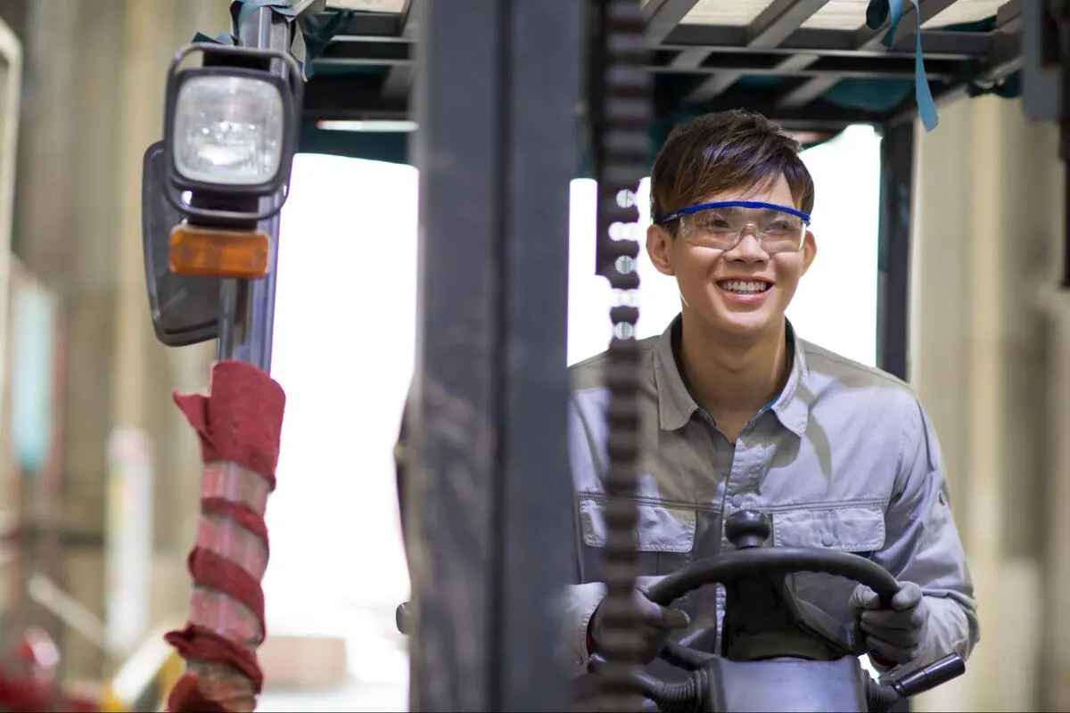 Forklift Operator Driving in Warehouse Singapore Young male forklift operator wearing safety glasses driving a forklift inside a warehouse in Singapore