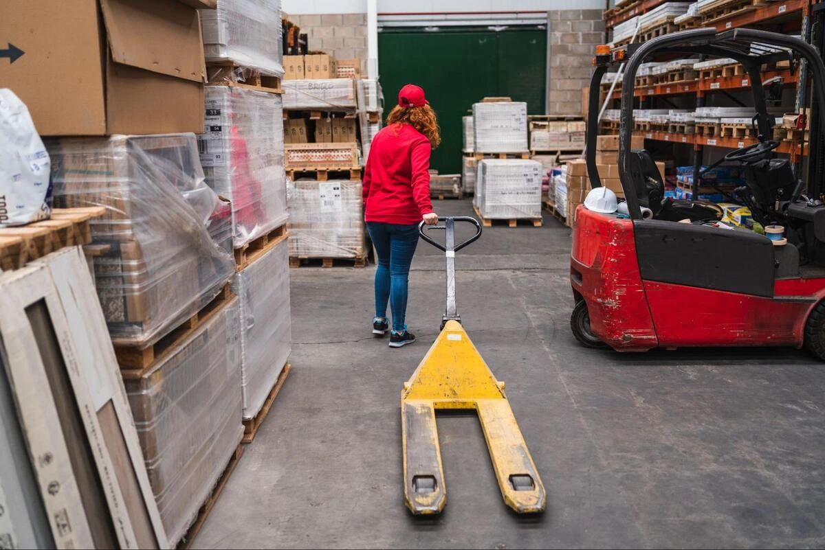Operating Electric Pallet Jack Safely Female warehouse employee operating an electric pallet jack near storage racks.