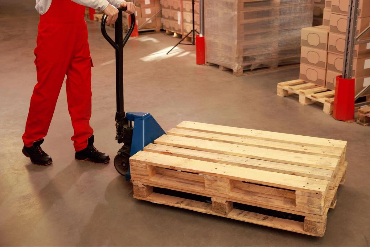 Moving Wooden Pallets in Warehouse Worker moving wooden pallets using a pallet truck.