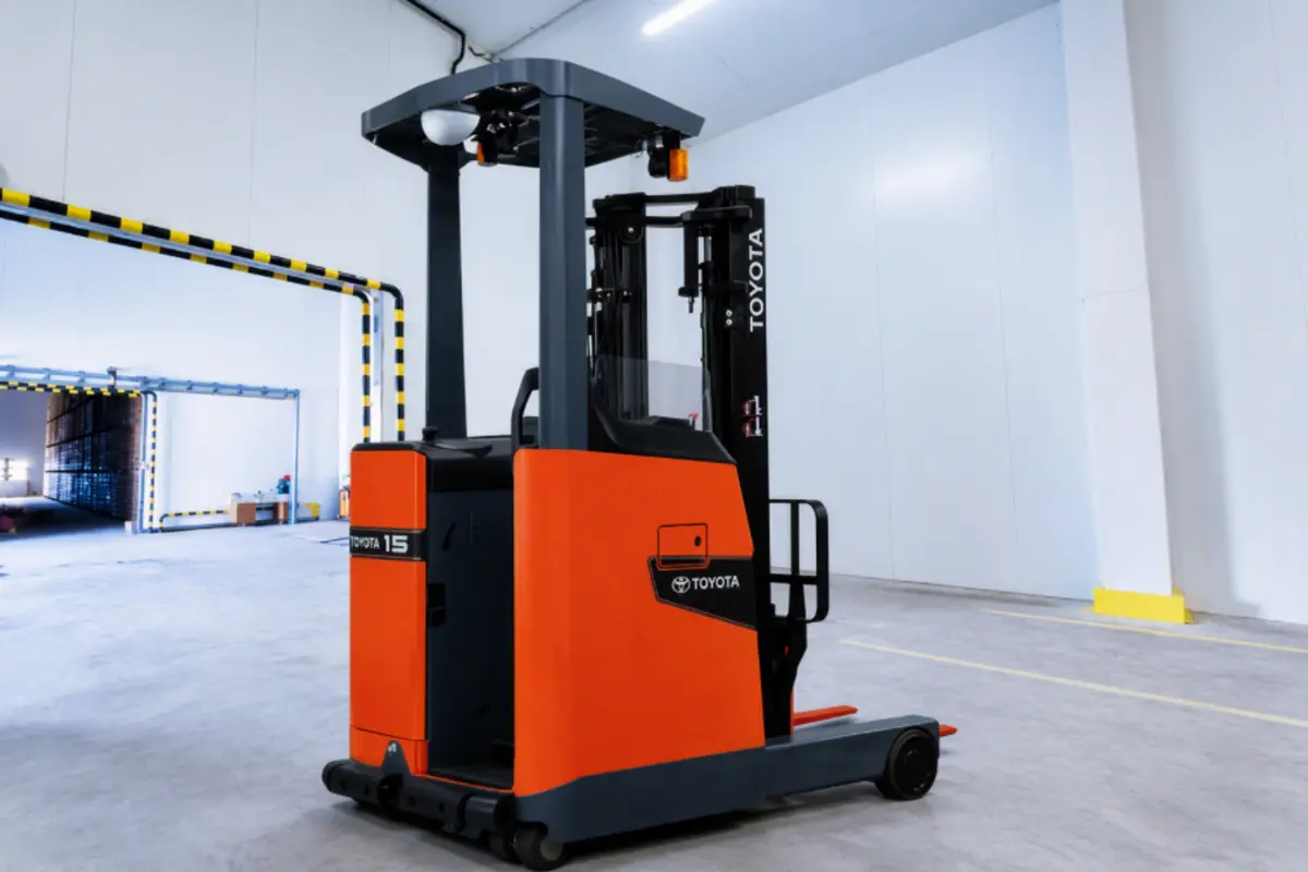 Rear view of a red and black electric reach truck parked in a warehouse aisle with yellow hazard-striped railings